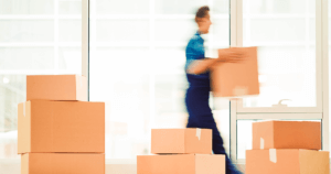 Image of room full of moving boxes with man in background walking holding a box